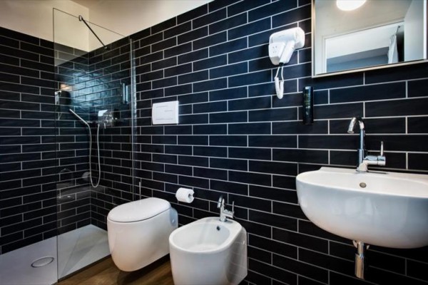 Moderní koupelna s tmavými obklady zahrnující sprchový kout, toaletu, bidet a umyvadlo.