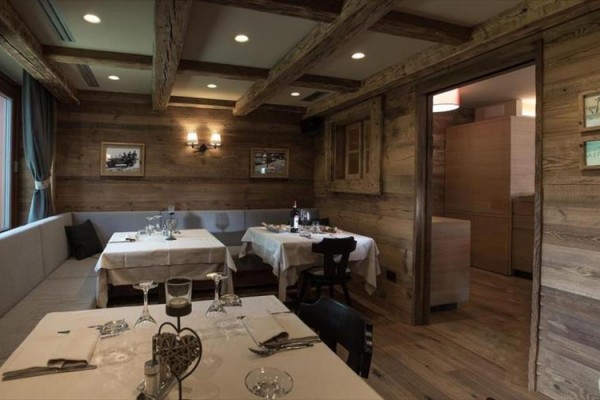 Restaurace s dřevěnými stěnami, stropními trámy a prostřenými stoly.