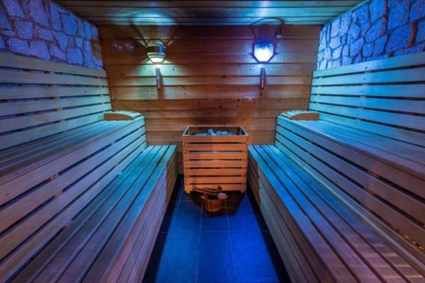 Dřevěná sauna s lavicemi, kamny a modrým osvětlením.  