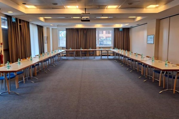 Konferenční místnost s uspořádáním stolů do tvaru U a lahvemi vody na každém stole.  