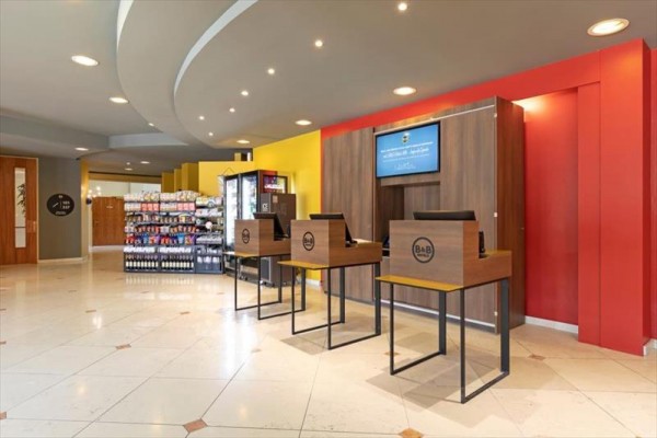 Hotelová recepce se samoobslužnými kiosky a regály se zbožím.