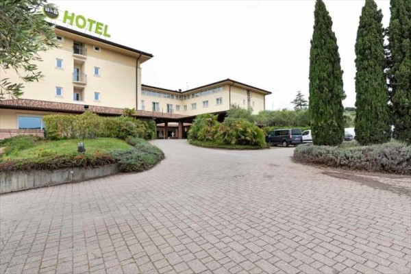 Velká budova hotelu se zelení a parkovištěm.