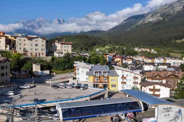 Horská vesnice s lanovkou a horami v pozadí.