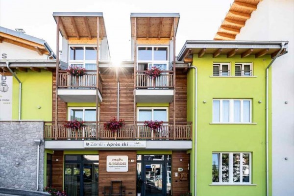 Budova s dřevěnými prvky a zelenou fasádou, s květinami na balkonech.