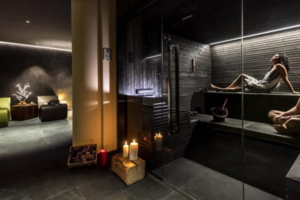 Lidé relaxující v moderní sauně s tlumeným osvětlením a svíčkami.