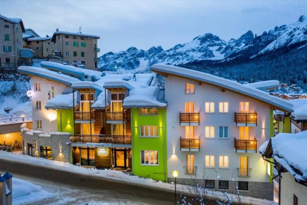Sněhem pokrytý horský hotel s dřevěnými balkony v zimní krajině.  