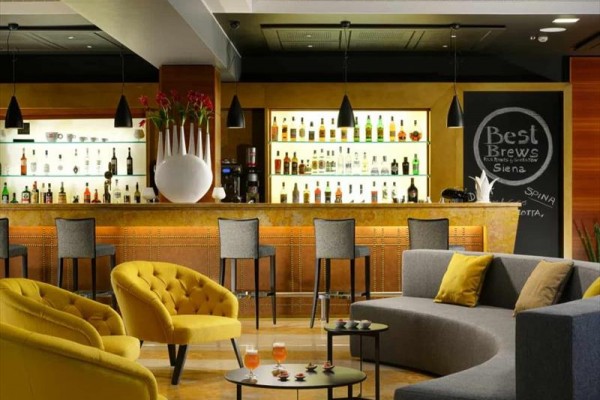 Elegantní hotelový bar s moderními sedacími soupravami a výběrem alkoholických nápojů na policích.