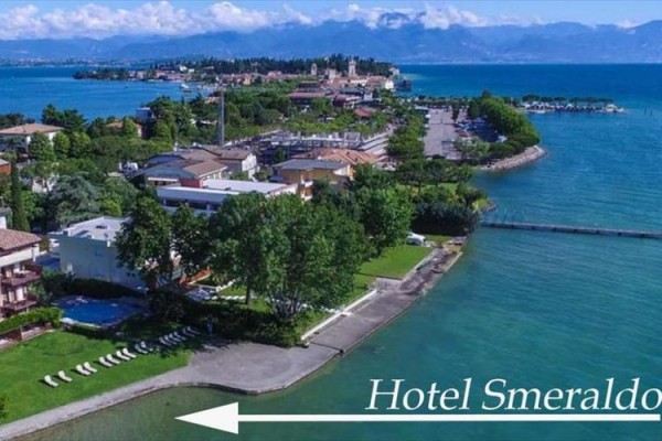 Pohled na pobřeží se zelení a budovami u jezera s označením Hotel Smeraldo.