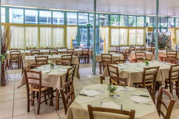Restaurace s dřevěnými židlemi a stoly s krémovými ubrusy.
