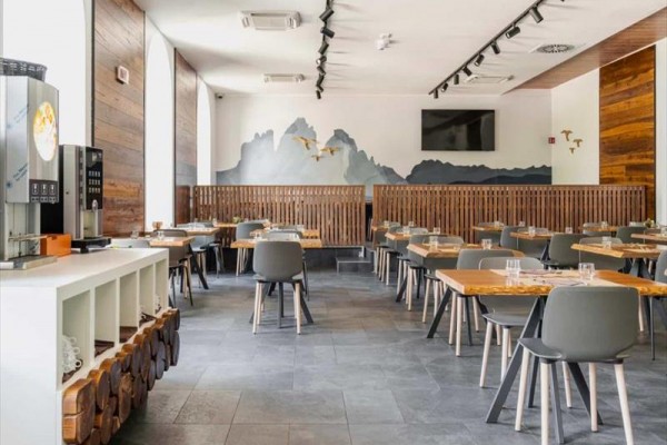Moderní restaurace s dřevěnými stoly a stěnou s vyobrazením hor a ptáků.