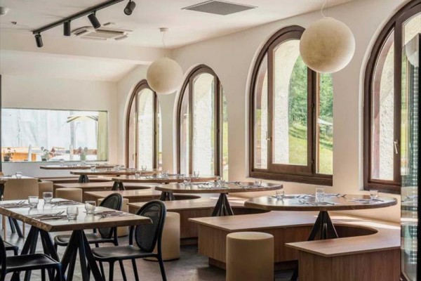 Moderní restaurace s velkými obloukovými okny a kulatými stoly.