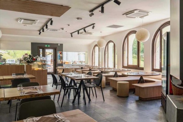 Moderní restaurace s prosklenými dveřmi a dřevěnými stoly.