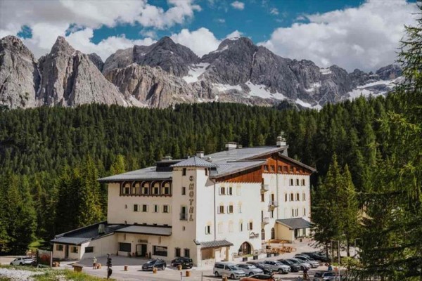 Hotel obklopený lesem s horským masivem v pozadí.