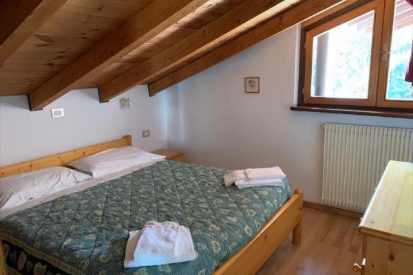 Podkrovní pokoj s manželskou postelí a dřevěným nábytkem.
