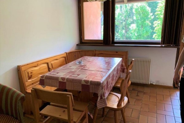 Jídelní kout s dřevěným stolem a židlemi u okna s výhledem na stromy.