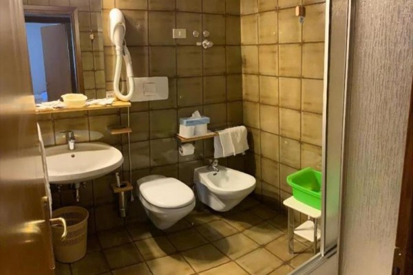 Koupelna s umyvadlem, toaletou, bidetem a sprchovým koutem, hnědé dlaždičky na stěnách.