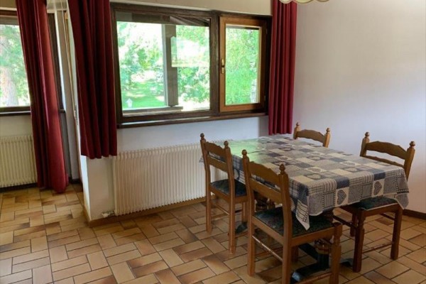 Jídelní stůl se čtyřmi židlemi a kostkovaným ubrusem vedle okna s červenými závěsy.