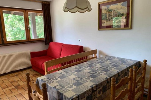 Pokoj s červenou pohovkou, dřevěným stolem a židlemi, s oknem a závěsy.