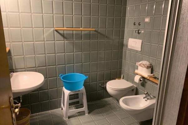 Koupelna s umyvadlem, toaletou, bidetem a modrým plastovým kýblem na stoličce.