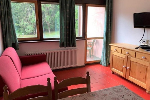 Obývací pokoj s červenou pohovkou, dřevěným nábytkem a velkými okny s výhledem do zahrady.