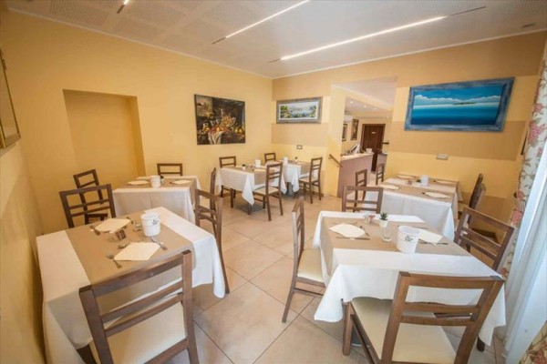 Světlá restaurace s dřevěnými židlemi a stoly prostřenými bílými ubrusy.