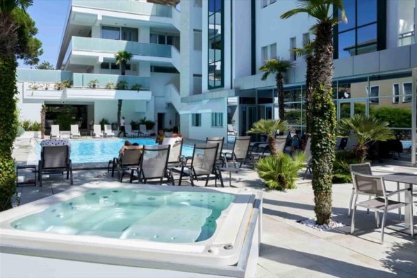 Moderní hotel s bazénem, vířivkou a venkovním posezením obklopený palmami.