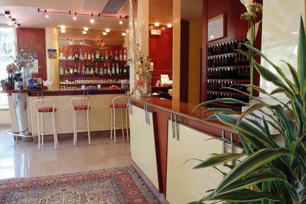 Interiér baru s pultem, židlemi a lahvemi alkoholu na pozadí.