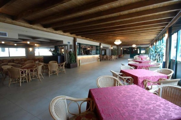 Velká restaurace s ratanovými židlemi a stoly s červenými ubrusy.
