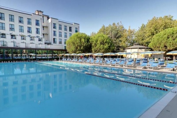 Velký venkovní bazén obklopený lehátky a slunečníky u moderního hotelu.