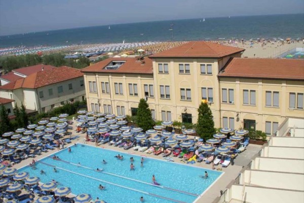 Hotel s bazénem a pláží v pozadí.
