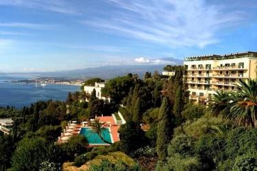 Hotel s bazénem obklopený stromy s výhledem na pobřeží a moře.