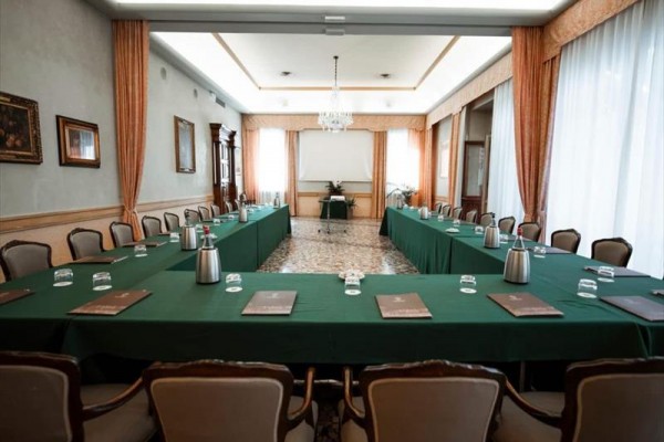 Konferenční místnost s uspořádáním do tvaru U, zelenými ubrusy a židlemi kolem stolů.