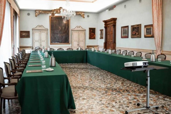 Konferenční místnost s uspořádáním do tvaru U, zelenými ubrusy a projektorem.