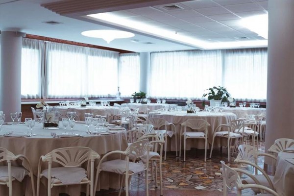 Elegantní restaurace s kulatými stoly a bílými židlemi připravená pro hosty.