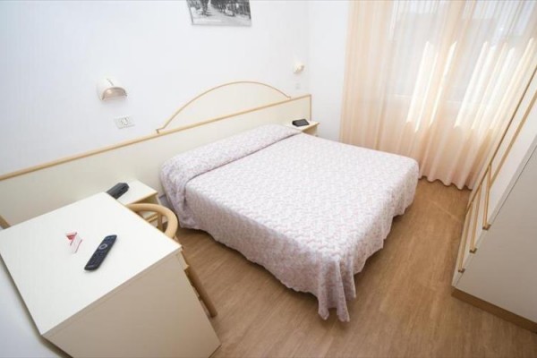 Světlý pokoj s manželskou postelí, stolem a židlemi.