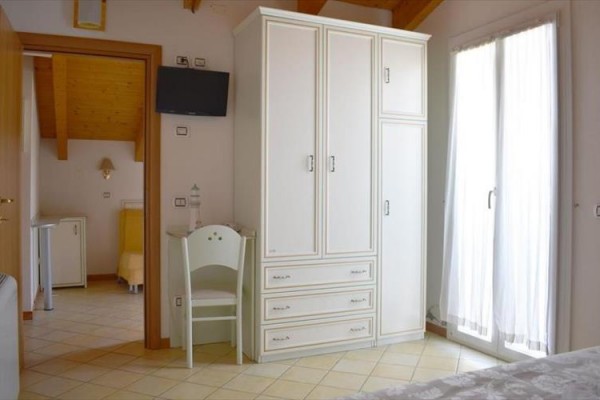 Světlý pokoj s bílou skříní a televizí na stěně vedle dveří na balkon.  