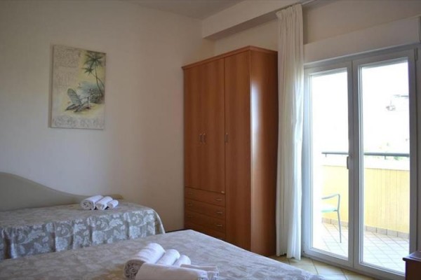 Ložnice se dvěma postelemi, skříní a otevřenými dveřmi na balkon.