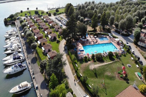 Letecký pohled na kemp s bungalovy, bazénem a parkujícími loděmi u vody.  