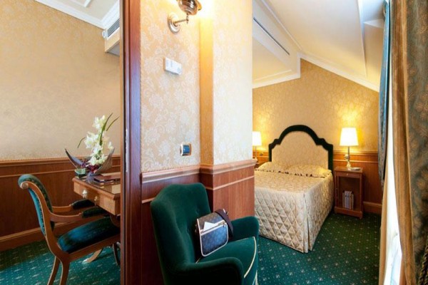 Elegantní hotelový pokoj s manželskou postelí a pracovním stolem.