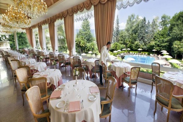 Elegatní restaurace s kulatými stoly a výhledem na zahradu s bazénem.