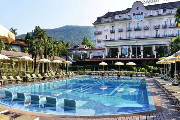 Hotel s venkovním bazénem a lehátky, v pozadí zelené hory.