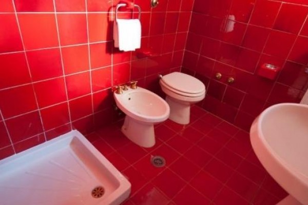 Koupelna s červenými kachličkami, obsahující sprchu, bidet, toaletu a umyvadlo.