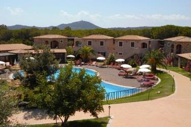 Prázdninový resort s bazénem obklopený zelení a horami v pozadí.