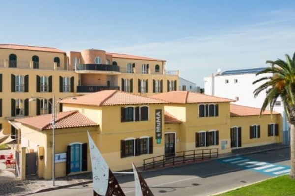 Historická budova s palmou a moderními sochami v popředí.