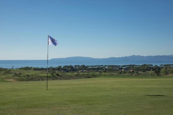 Golfové hřiště s výhledem na moře a hory v pozadí.