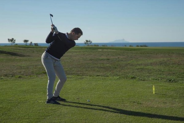 Muž na golfovém hřišti se chystá odpálit míček.