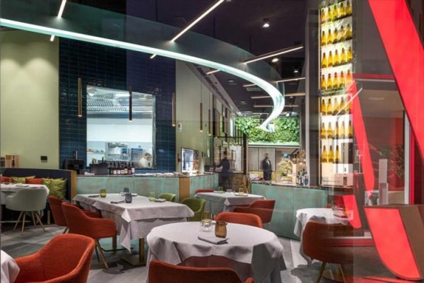 Moderní restaurace s barevnými židlemi a zakřivenou světelnou instalací.