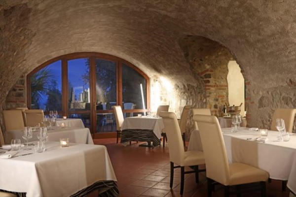 Restaurace v kamenném sklepě s bílými ubrusy a zapálenými svíčkami.