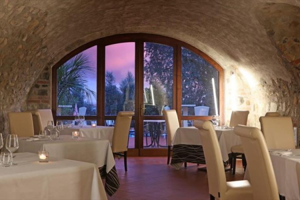Interiér restaurace s obloukovými okny a výhledem na krajinu při západu slunce.