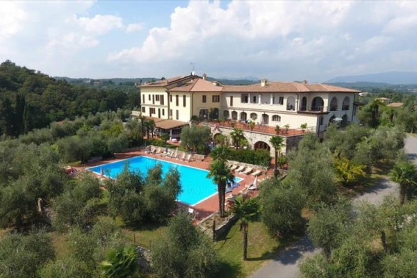 Hotel s bazénem obklopený olivovníky a zelení v venkovské krajině.